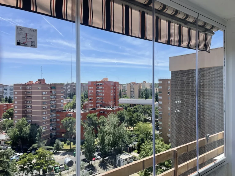 Paneles de cristal en un balcón con toldo rayado y vistas urbanas