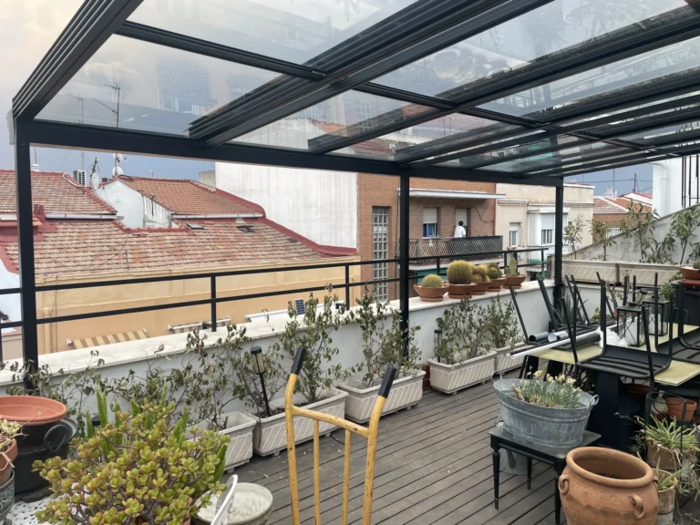Cubierta de cristal con estructura oscura sobre una terraza con plantas