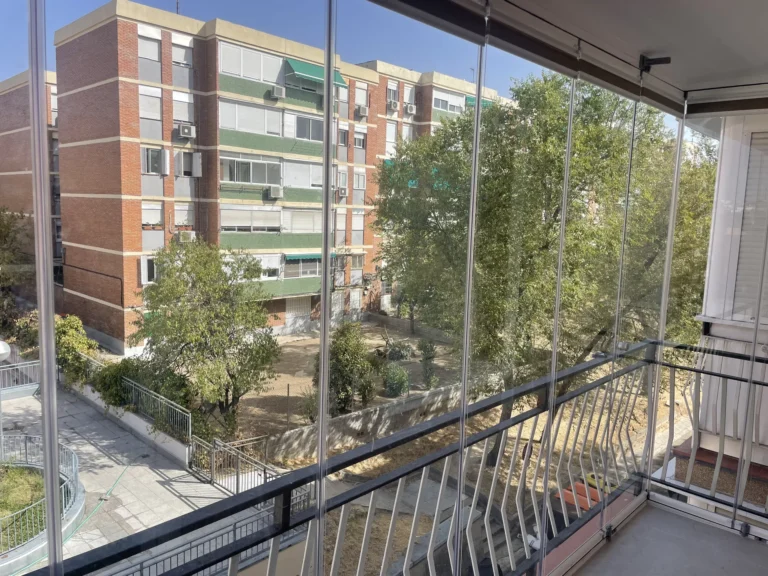Frente de balcón con cortinas de cristal y vistas a una zona residencial