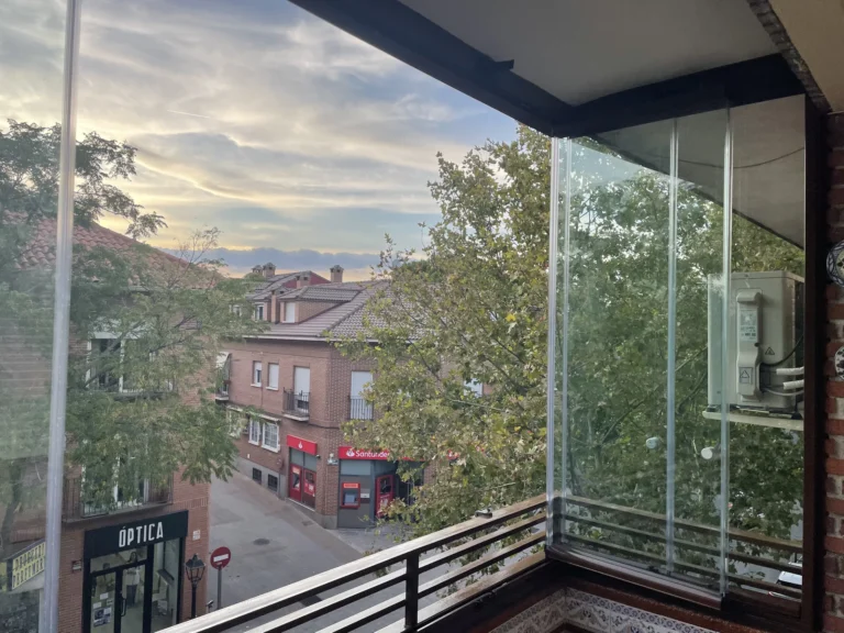 Esquina de balcón con paneles de cristal y vistas a una calle