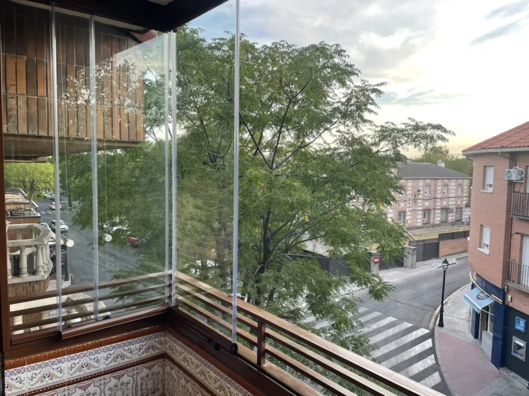 Frente acristalado de un balcón con árboles y edificios al fondo