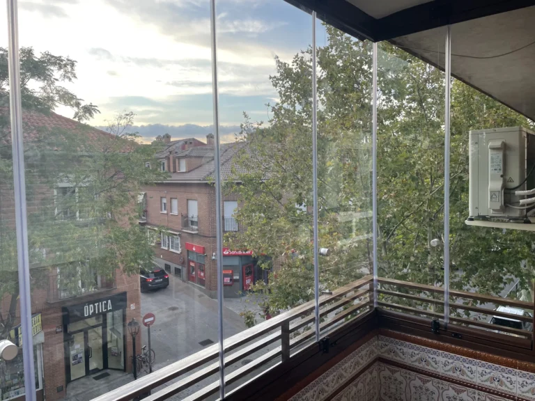 Lateral de un balcón acristalado con vistas a árboles y edificios