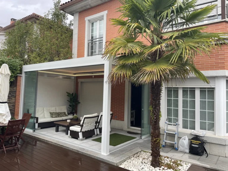 Pérgola blanca adosada a una casa con cerramiento lateral de cristal