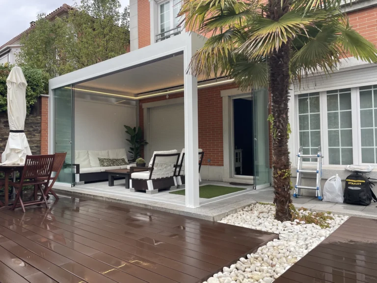 Zona de estar bajo una pérgola blanca con paneles laterales de cristal