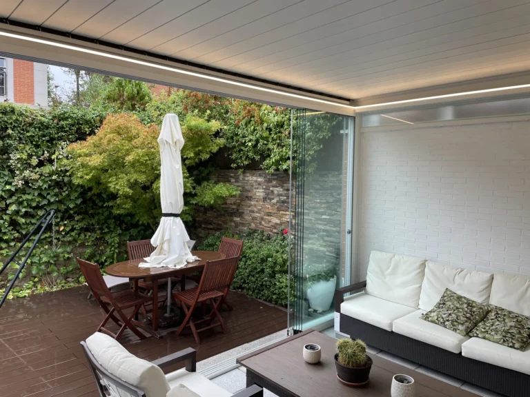 Interior de una pérgola con cubierta blanca, iluminación y paneles laterales de cristal